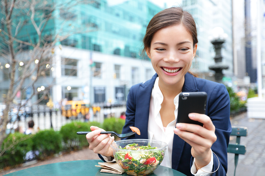 Joven mujer de negocios comiendo ensalada en el almuerzo en City Park viviendo un estilo de vida saludable trabajando en un teléfono inteligente.  Feliz sonriente joven empresaria multirracial, Bryant Park, Manhattan, Ciudad de Nueva York, EE.UU.